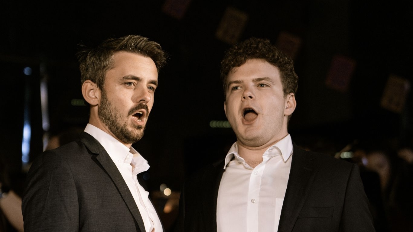 a photo of Chris Murphy and Andrew Randell standing side to side in formal suits singing in Opera on locations produciton of Verdi's A Masked Ball